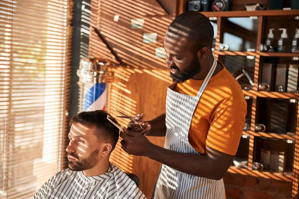 Veselý holič stříhání klientských vlasů s nůžkami v holičství — Stock fotografie