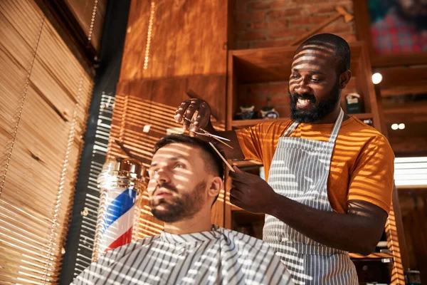 Barbeiro sorridente corte de cabelo do cliente com tesoura na barbearia — Fotografia de Stock