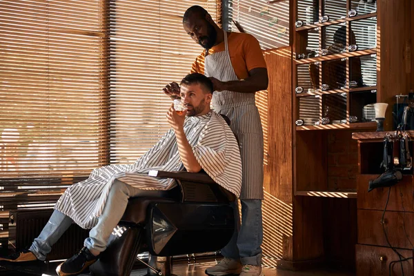Barbeiro em avental de corte de cabelo do cliente com tesoura — Fotografia de Stock