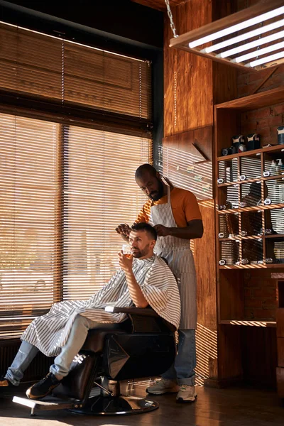 Vousatý holič stříhání klientské vlasy s nůžkami — Stock fotografie