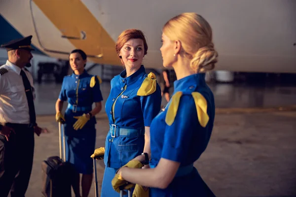 Schöne kaukasische Stewardessen stehen mit rollenden Taschen in den Innenräumen — Stockfoto