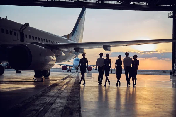 Professional pilots with stewardesses enjoying beautiful sunset at the aviation hangar — Stock Photo, Image