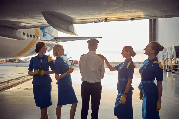 Hermosas mujeres azafatas en uniformes azules de pie con el capitán del avión bajo el ala de los aviones de pasajeros — Foto de Stock