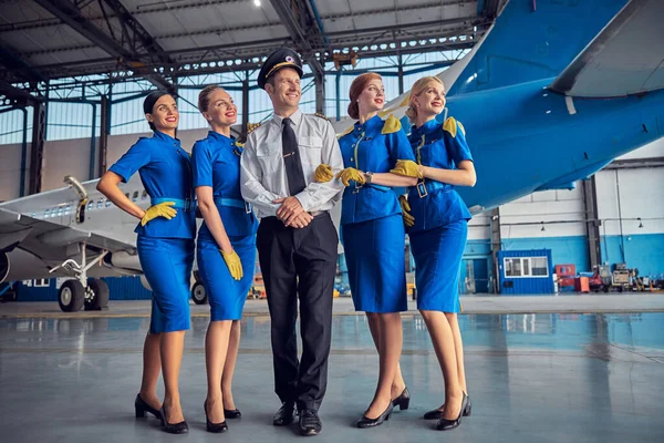 Улыбающиеся веселые четыре стюардессы с красивым пилотом в стильной форме — стоковое фото