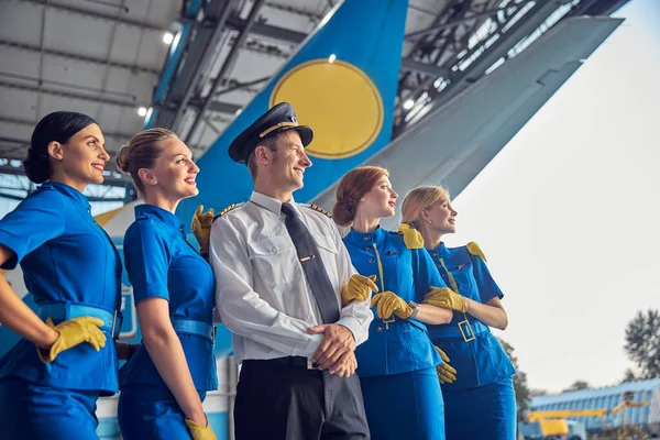 Piloto bonito e quatro aeromoças em uniforme elegante olhando para a distância — Fotografia de Stock