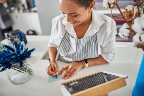 Een vrolijke dame die een pen vasthoudt en een briefje schrijft. — Stockfoto