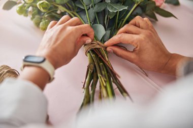 Bir demet çiçeğin etrafına kahverengi iplik bağlayan nitelikli bir çiçekçi.