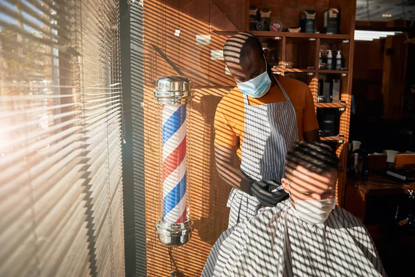 Frisör i medicinsk mask gör frisyr för man i frisör — Stockfoto