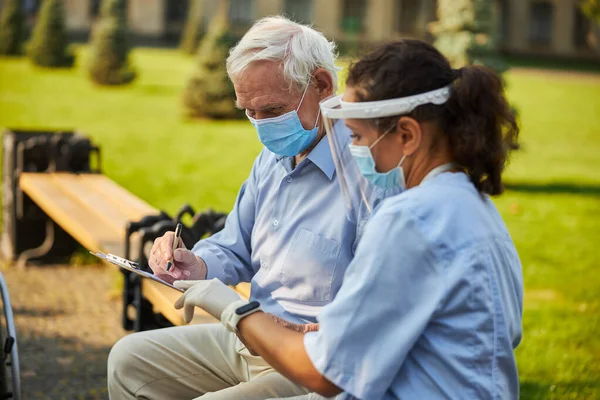 Verpleegster en oude patiënt op bank in de buurt van bejaardentehuis — Stockfoto