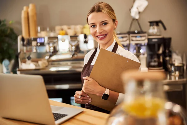 Jonge vrolijke ondernemer houdt klembord in de hand in het cafe — Stockfoto