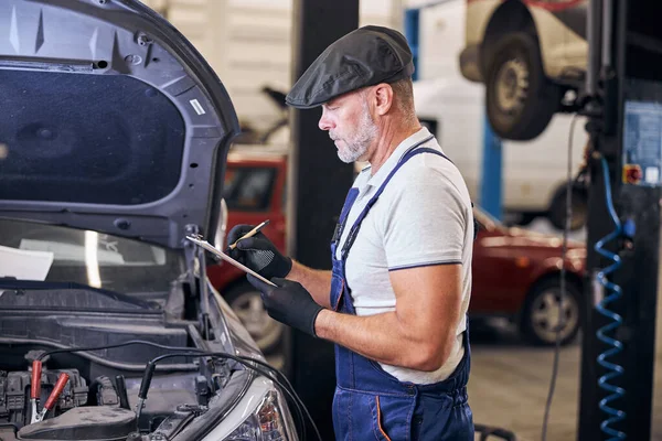 Bärtige männliche Arbeiter schreiben auf Klemmbrett in Auto-Reparatur-Station — Stockfoto