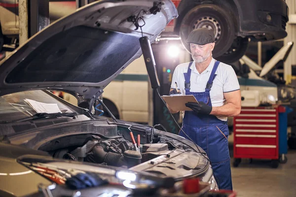 Bearded male worker writing on clipboard in service garage — Stock Photo, Image