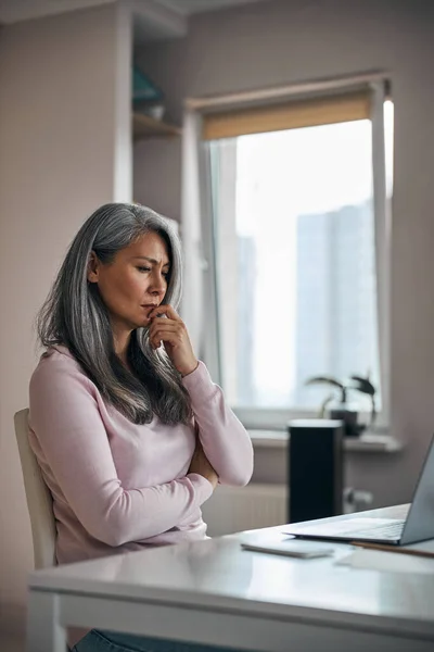 Opgewonden vrouw in blozen trui denken aan iets tijdens het zitten op de werkruimte — Stockfoto