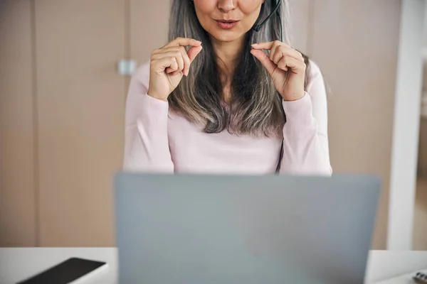 Grå hår kvinna gestikulerar vid kameran på datorn medan du sitter på kontoret — Stockfoto