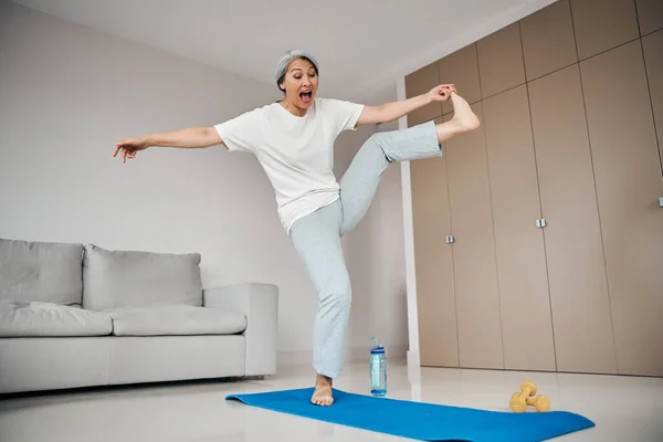 Donna felice divertente in piedi sul tappeto blu yoga in soggiorno a casa — Foto Stock