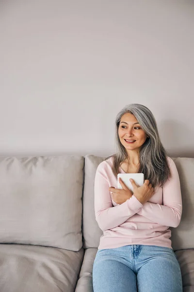 Hermosa asiática bonita dama mirando hacia otro lado mientras sentado en habitación interior aislado en gris fondo — Foto de Stock