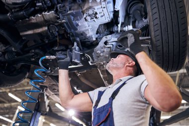 Sakallı erkek işçi garajda İngiliz anahtarı kullanıyor.