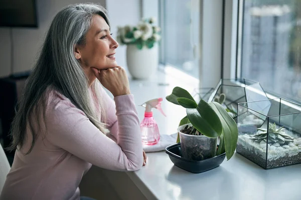 Mujer encantadora sentada en el alféizar de la ventana con plantas de interior — Foto de Stock