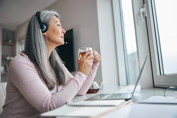 Charmig kvinna dricka te och använda laptop hemma — Stockfoto