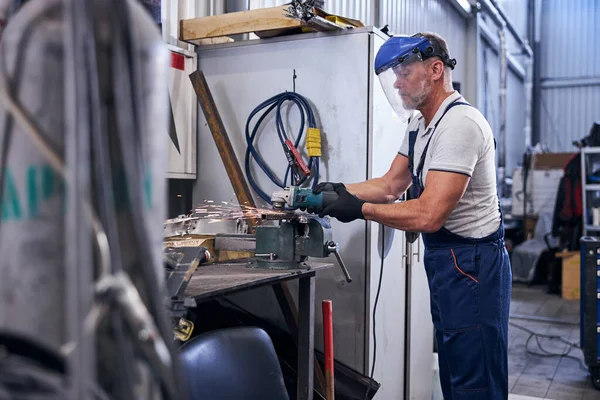 Mężczyzna pracownik w masce ochronnej za pomocą szlifierki w garażu — Zdjęcie stockowe