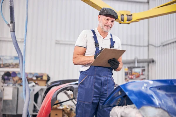 Guapo mecánico de la escritura en portapapeles en el taller de reparación de automóviles — Foto de Stock