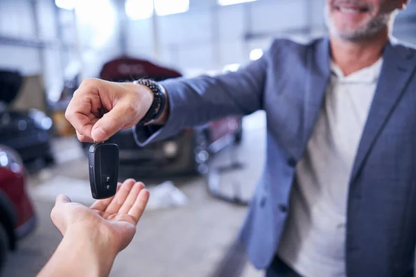 Homem alegre dando chave de carro inteligente para mecânico na estação de serviço — Fotografia de Stock