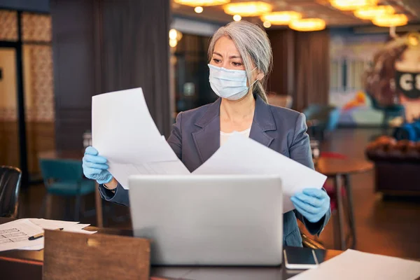 Жінка-архітектор в медичній масці вивчає документи на роботі — стокове фото
