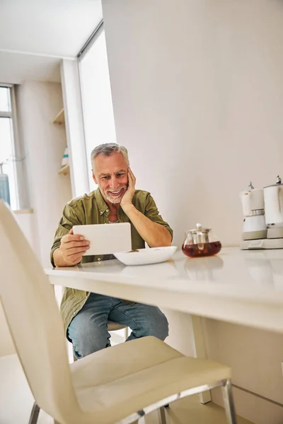 Улыбающийся пожилой джентльмен смотрит на экран планшета во время чая — стоковое фото