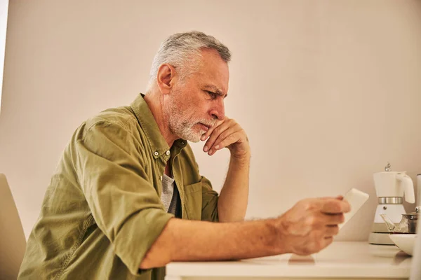 Concerned aging man checking his tablet and looking serious — Stock Photo, Image