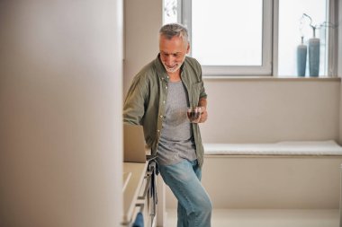 Çay içen ve bilgisayarını mutfakta kontrol eden yaşlı bir beyefendi.