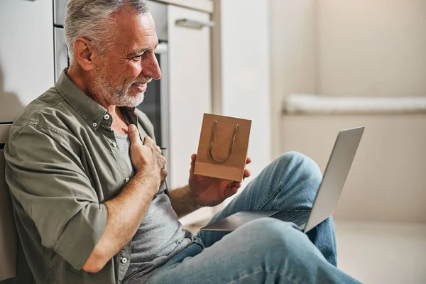 Благодарный пожилой мужчина с подарком и ноутбуком — стоковое фото
