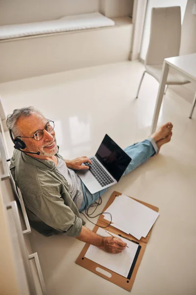 Busy senior citizen wearing headphones while working from home