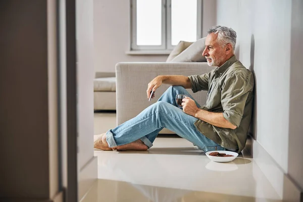 Grey-haired gentleman having tea with cookies on the floor — Stock Photo, Image