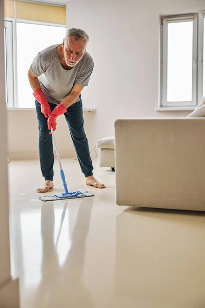 Verantwoordelijke oudere man die zijn vloer met een dweil schoonveegt — Stockfoto