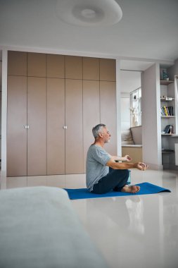 Yaşlı bir adam oturma odasında meditasyon yapıyor.