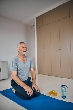 Yoga yapmaya evde odaklanmış yaşlı bir beyefendi.