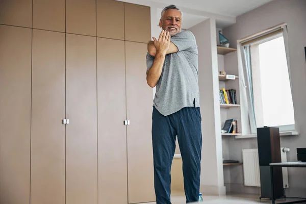 Aged man pressing on his elbow to stretch his arm — Stock Photo, Image