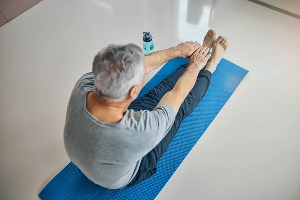 Caballero mayor estirándose sobre una esterilla de yoga —  Fotos de Stock