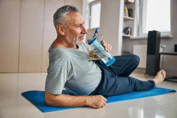 Aktif emeklinin evde egzersiz yaparken susuz kalması — Stok fotoğraf