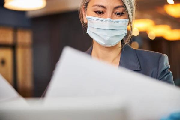 Бізнес-леді в медичній масці, що вивчає документи на роботі — стокове фото
