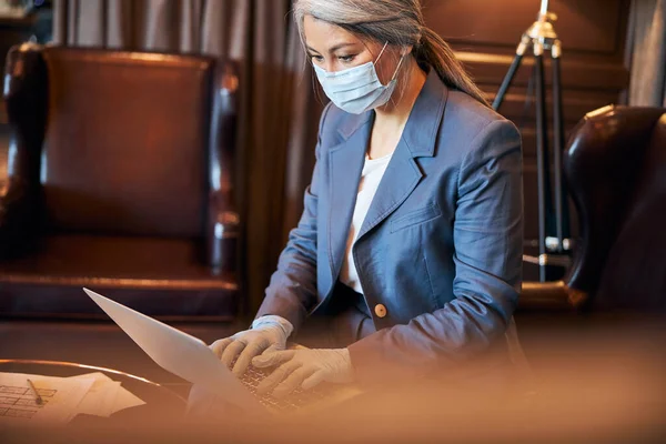 Елегантна жінка в медичній масці, що працює на ноутбуці — стокове фото