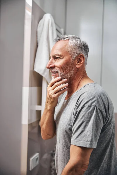 Ένας χαμογελαστός ηλικιωμένος κύριος κοιτάζει τα γένια του στον καθρέφτη. — Φωτογραφία Αρχείου