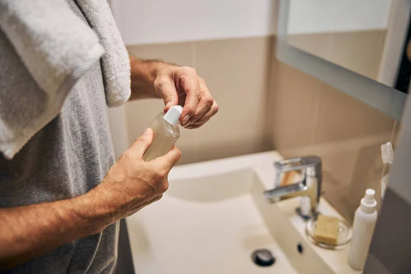 Чоловік у ванній відкриває пляшку з миттям тіла — стокове фото