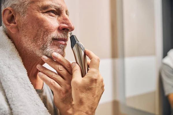 Smiley senior man grooming his nose hair with a trimmer — Stock Photo, Image