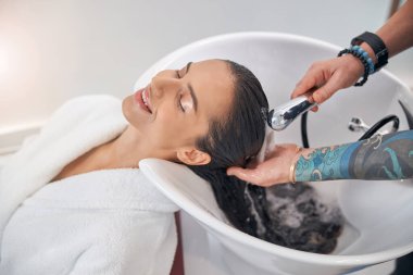 Köpük, temiz, siyah saçlardan aşağı akıyor.