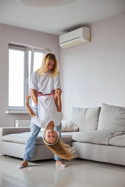 평범 한 옷을 입은 성인 여성이 어린 여자 아이를 다리로 안고 방 안에서 즐거운 시간을 보내는 모습 — 스톡 사진