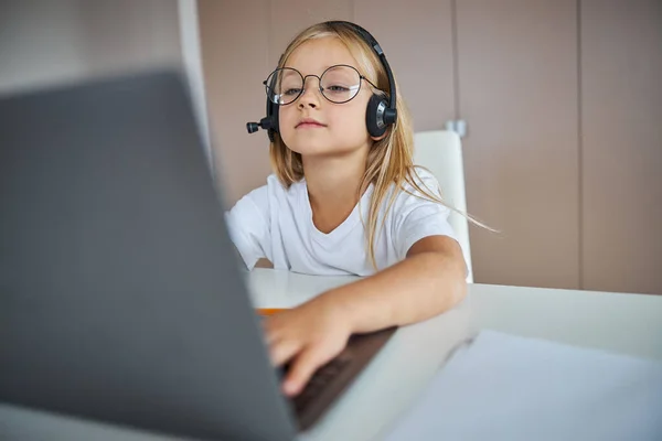 Charming little miss in eyeglasses looking to the screen laptop in her room — Stock Photo, Image