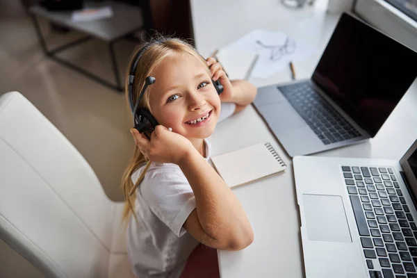 Happy smiling little miss in headphones sitting at the work desk in room inside — Stock Photo, Image