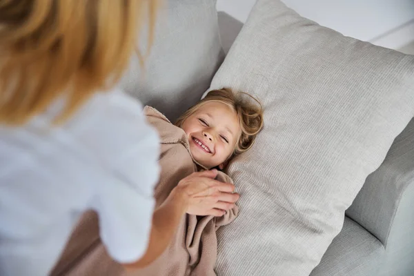 Feliz niña sonriente tumbada en el sofá mientras se siente bien cerca de su madre — Foto de Stock