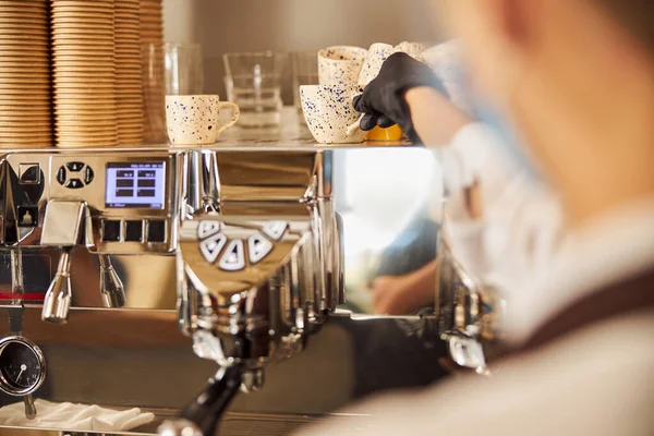 Жіноча рука в гумовій рукавичці бере чашку чашки з підігрівом лотка в кафе — стокове фото